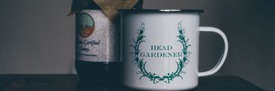 white head gardener ceramic cup near glass jar on brown panel